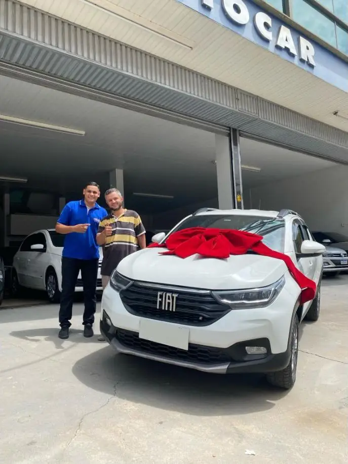 Lucas e cliente com uma Fiat Strada branca com laço vermelho